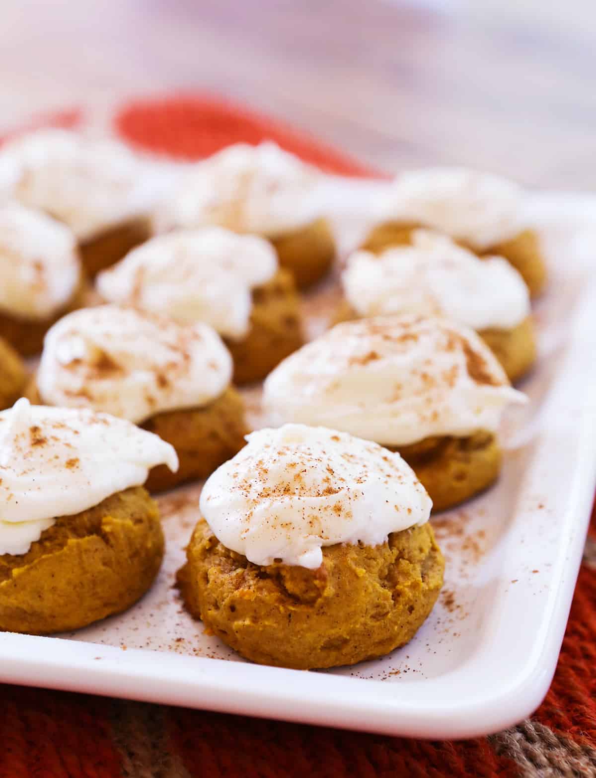 platter of perfectly lined up pumpkin cookies and frosting on top.