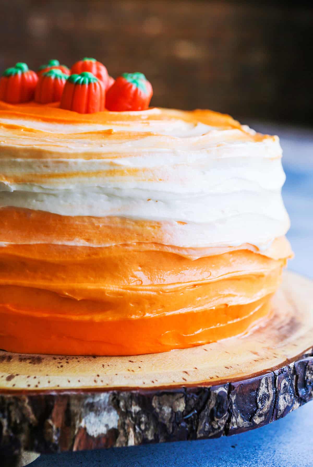 Close up of an ombre decorated layer cake with orange and white frosting and candy pumpkins on top.