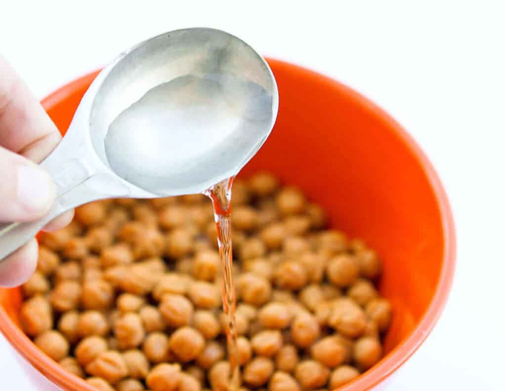 A tablespoon pouring water into a bowl of caramel bits.