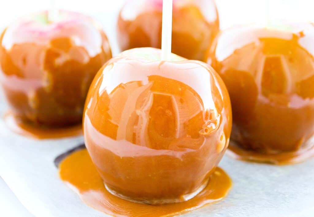 4 caramel apples sitting on parchment paper.