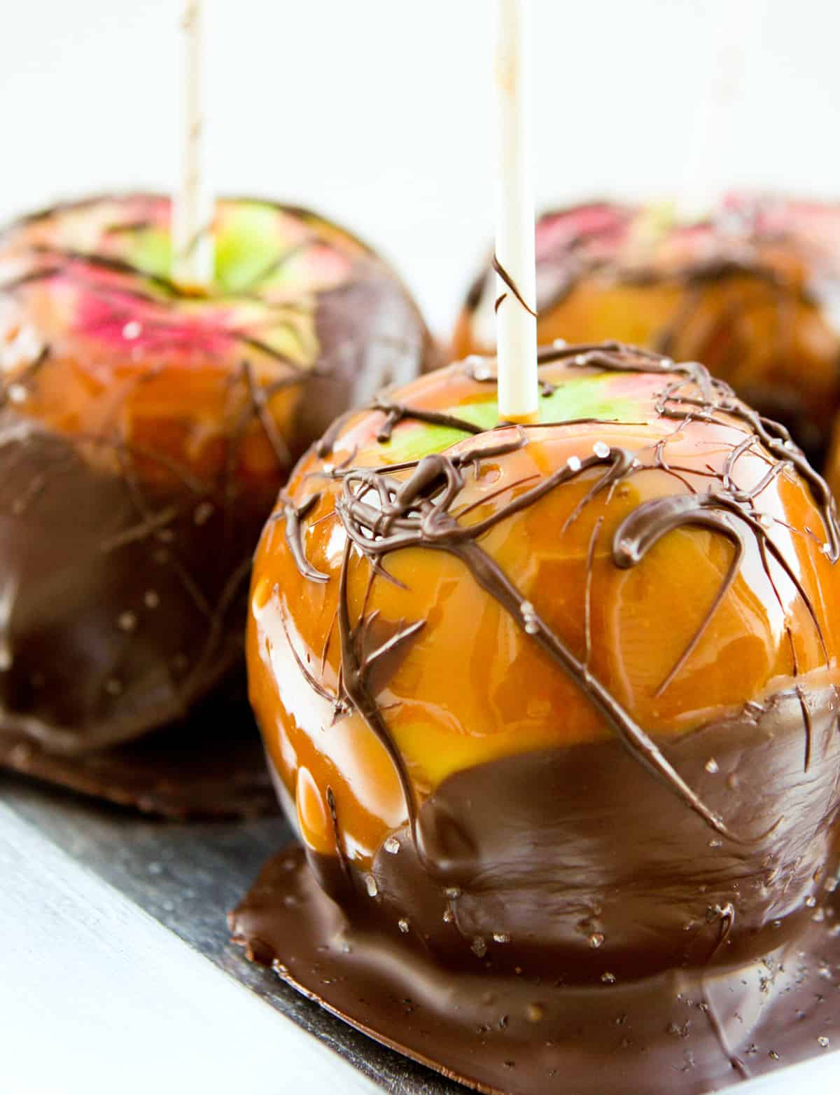  Close up of caramel apple dipped in chocolate with sea salt sprinkled around it.