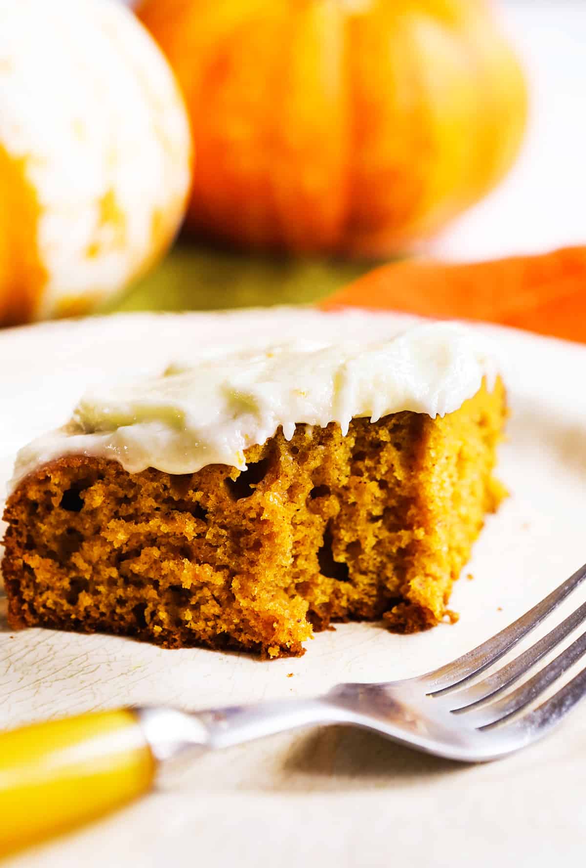 close up slice of a pumpkin bar with a bite taken out of it and a fork in front of it. 
