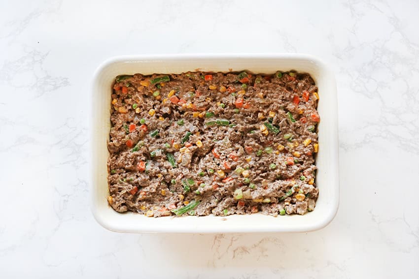 Homemade beef and vegetable meatloaf in a white baking dish, ready to bake or serve.