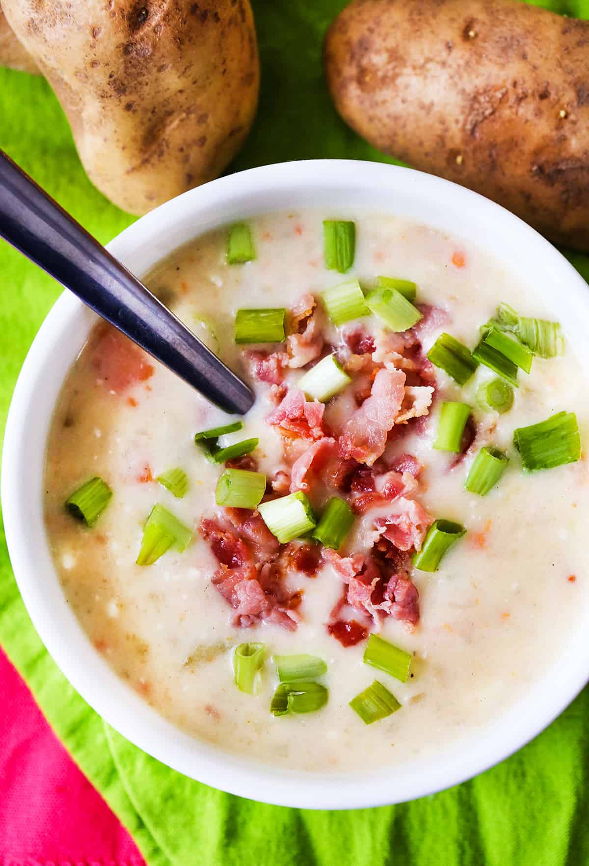 Top view of a loaded bowl of potato soup, sitting next to 2 russet potatoes.