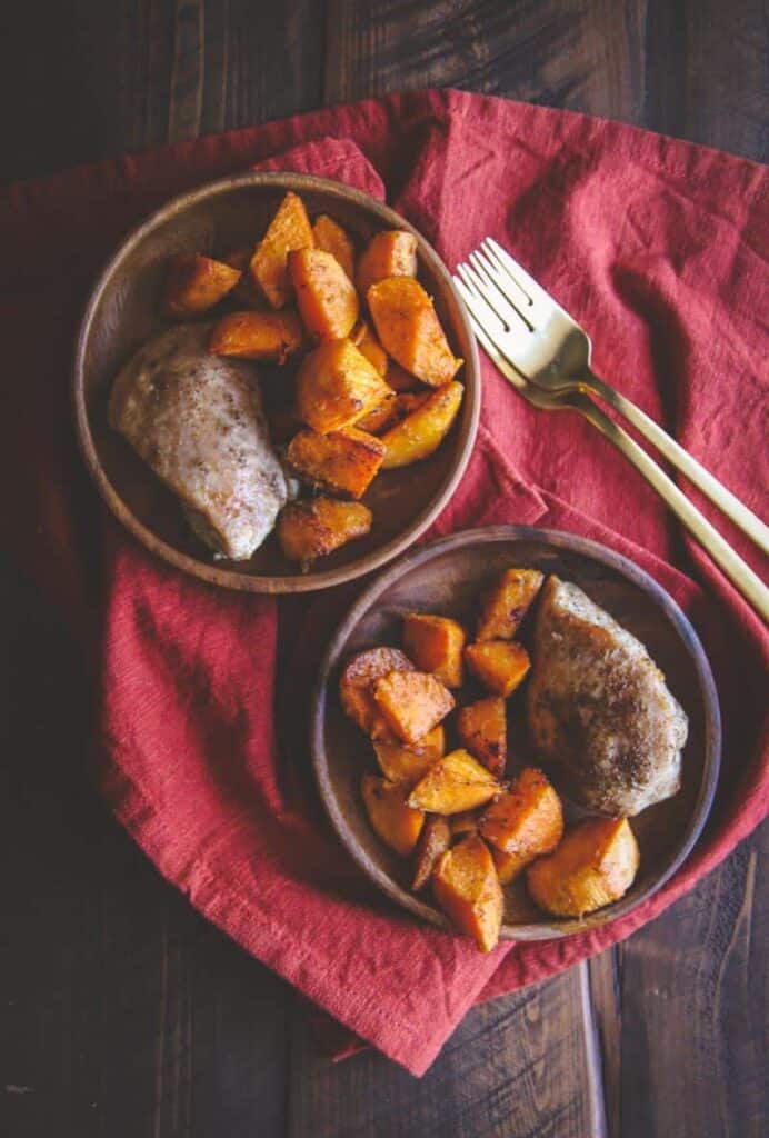 Two bowls each filled with a serving of sweet potatoes and chicken ready to eat with forks alongside. 