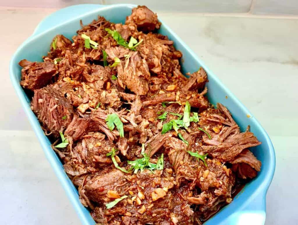 A casserole dish of instant pot barbacoa cooked and ready to serve. 