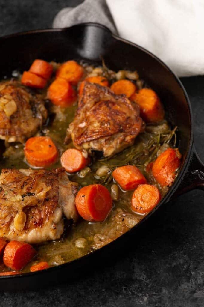 Chicken in white wine with cooked carrots ready to serve from a cast iron skillet