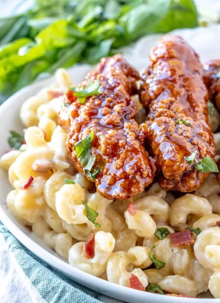 A platter of mac and cheese with 2 honey pepper chicken strips on top. 