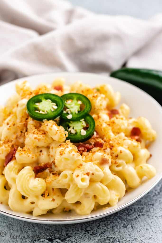 Bowl of mac and cheese with bacon in it and jalapeno slices over the top. 