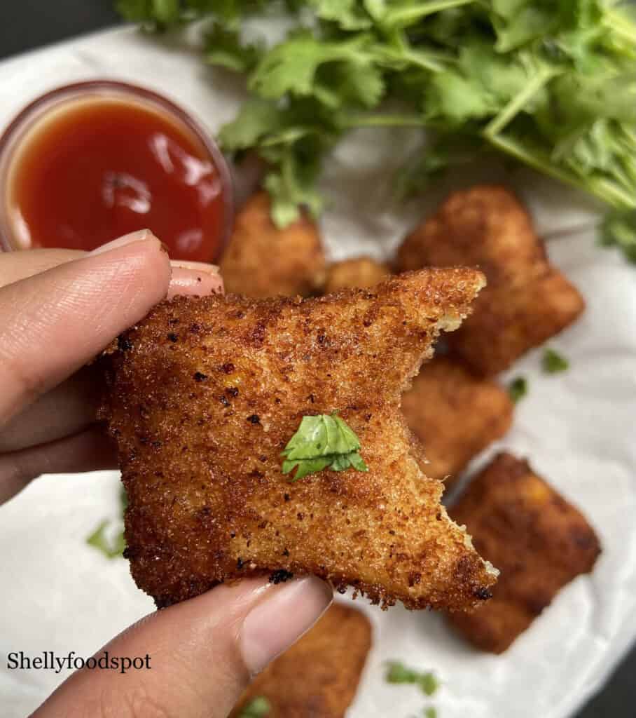 Hand holding a cheese corns nugget with a bite missing. 