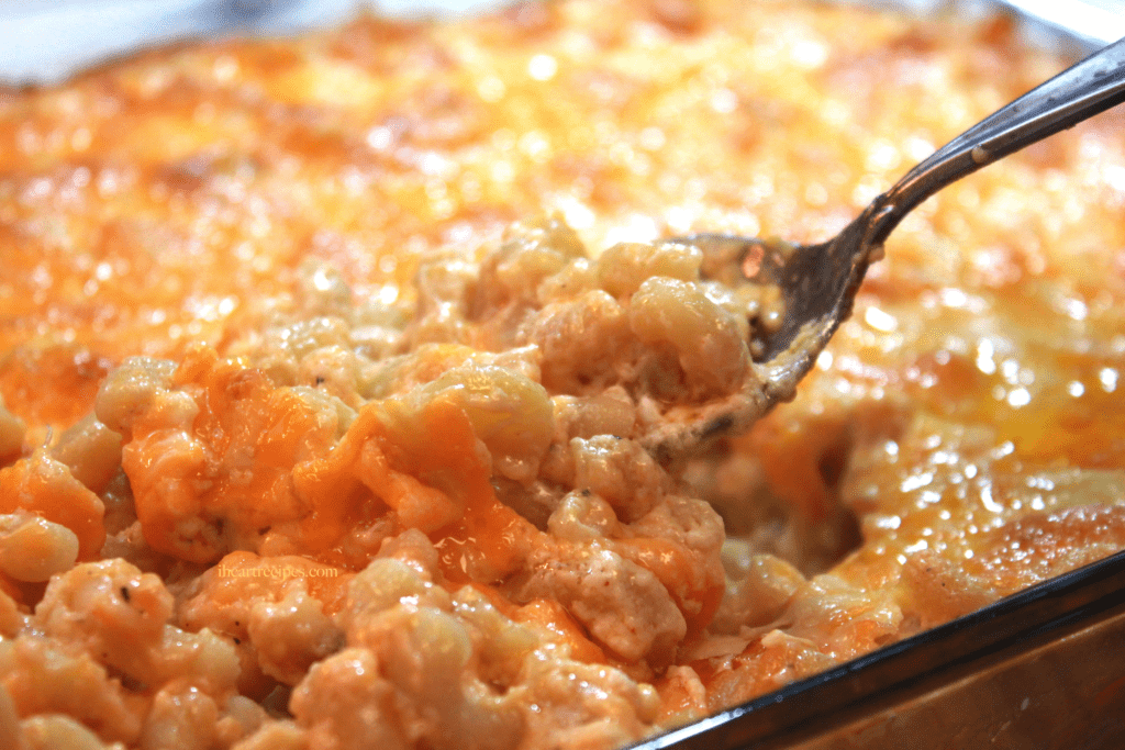 A spoon inside a casserole pan of hot melted soul food macaroni and cheese.
