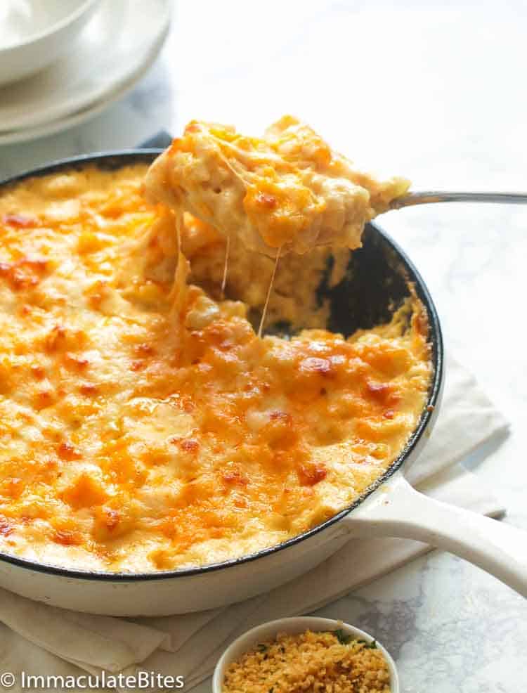 A skillet of mac and cheese with a serving spoon pulling up a scoop of it with melted cheese stringing down. 