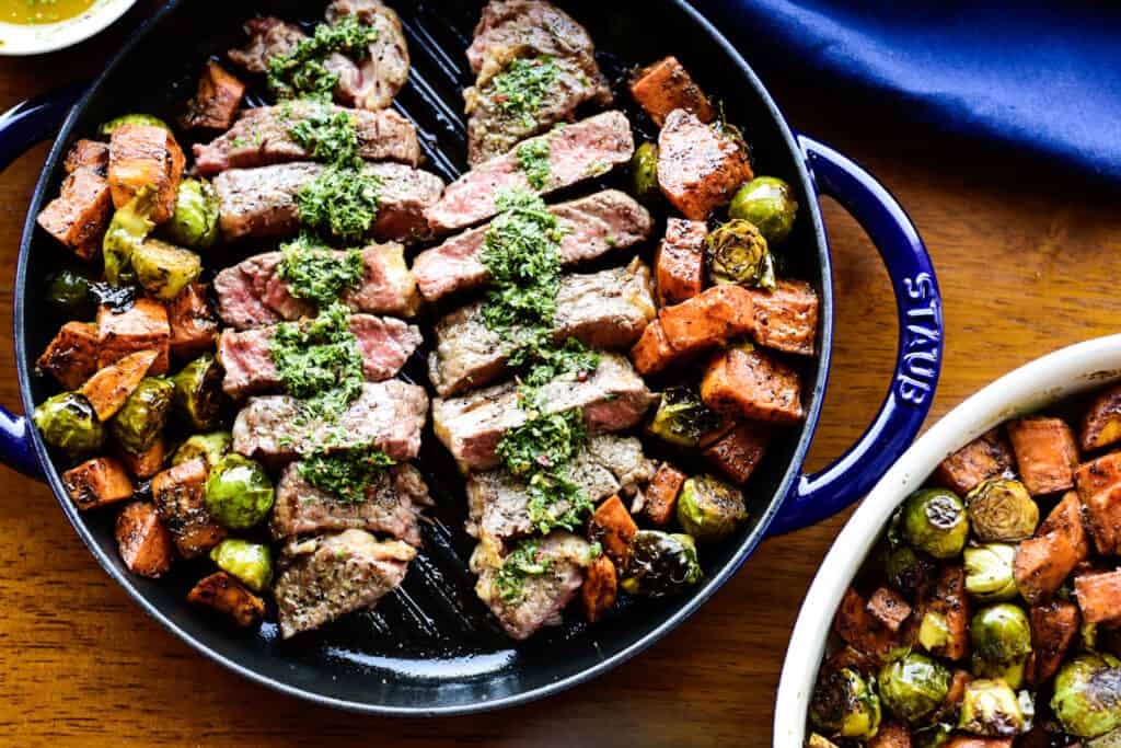 New York Strip Steak with Chimichurri Sauce in a grilled dish and veggies grilled alongside it. 