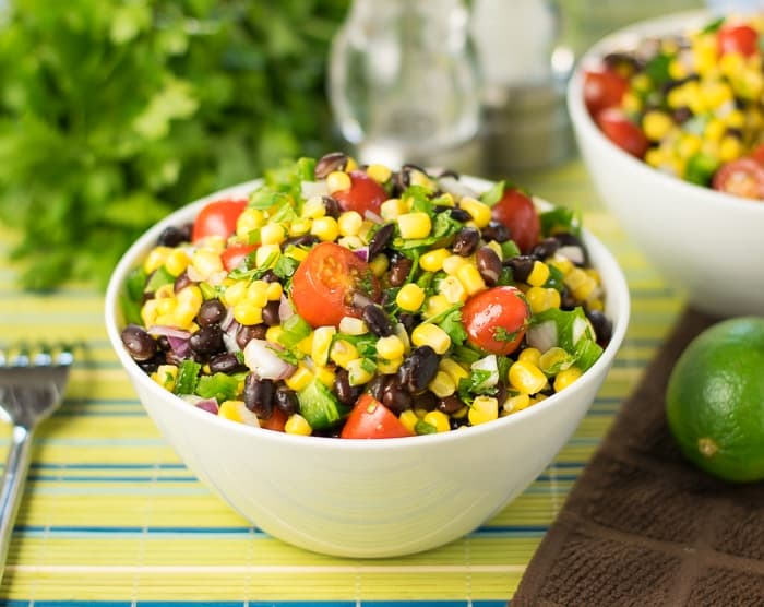 Full serving bowl of black beans and corn with lime juice on a table next to a fork.