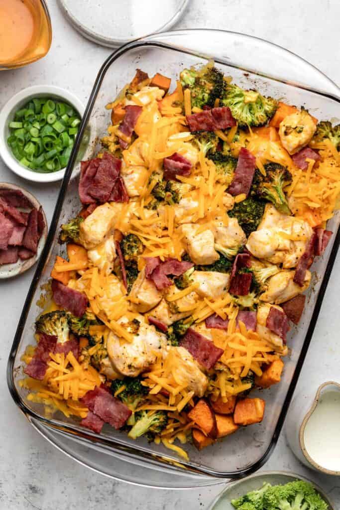 Glass casserole dish melted cheese on top of bacon, chicken pieces, broccoli florets and diced sweet potatoes. 