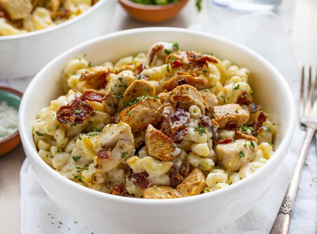 A bowl of chicken ranch and cacon macaroni and cheese with a fork sitting to the right of it. 