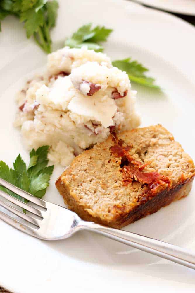 Feta and sun-dried tomato turkey meatloaf on a plate with a scoop of mashed potatoes next to it with a garnish of parsley.  