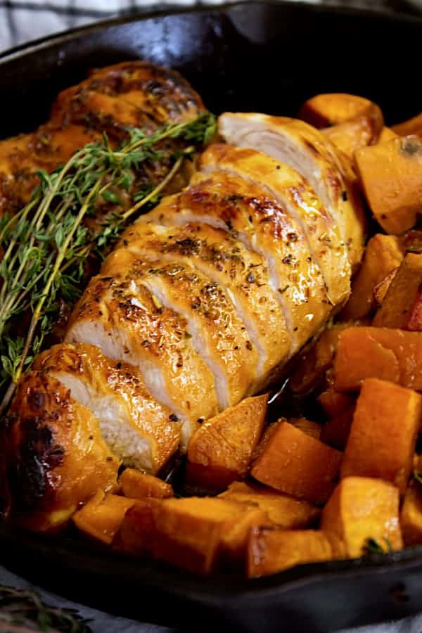 A piece of chicken with honey glaze on a platter with sprigs of thyme and diced sweet potatoes, ready to be dished up.