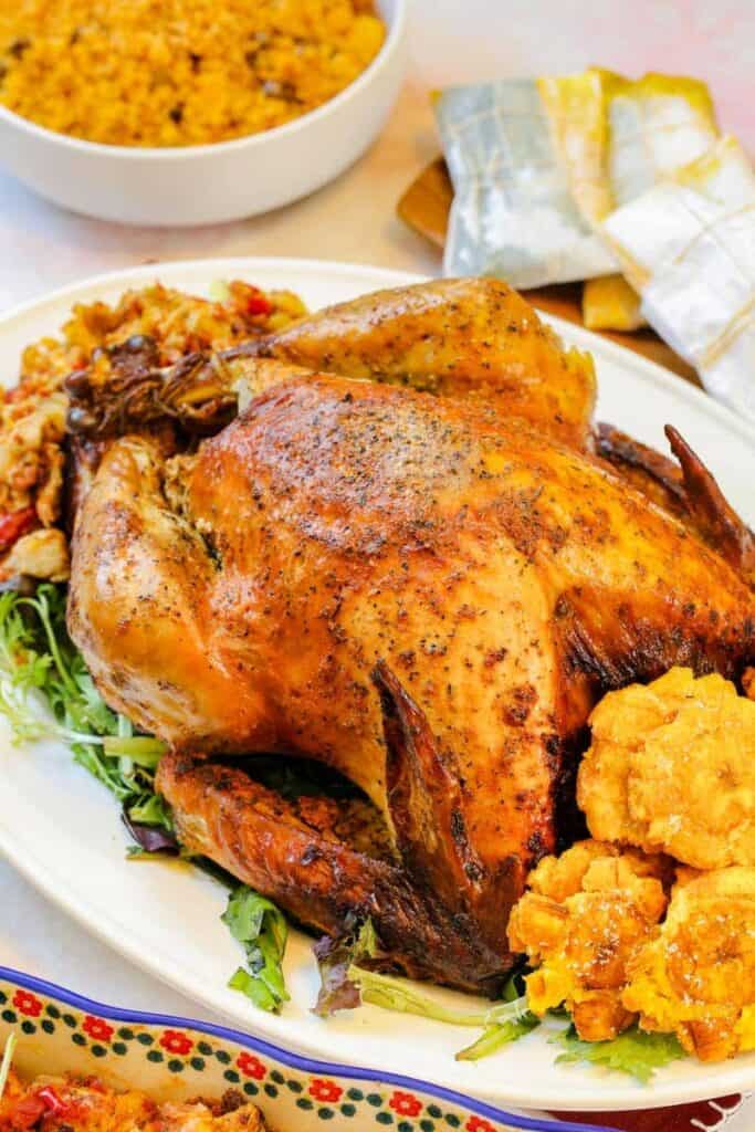 Baked turkey with seasonings and veggies sitting on a plate, ready to be carved and served. 