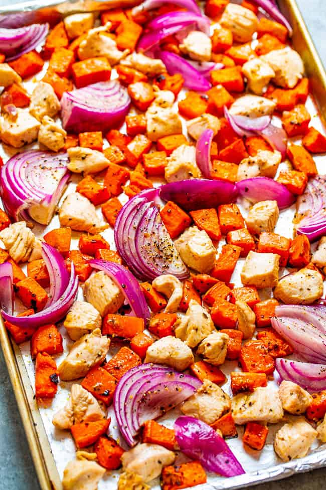 A sheet pan full of sweet potatoes diced up and red onions sliced up with chicken bites mixed in. 