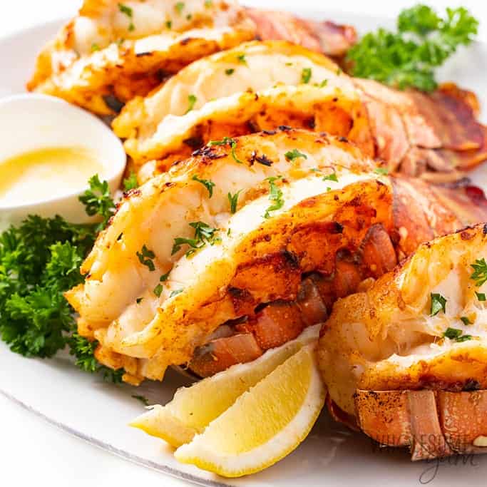 Lobster tails on a plate with melted butter and lemon slices. 