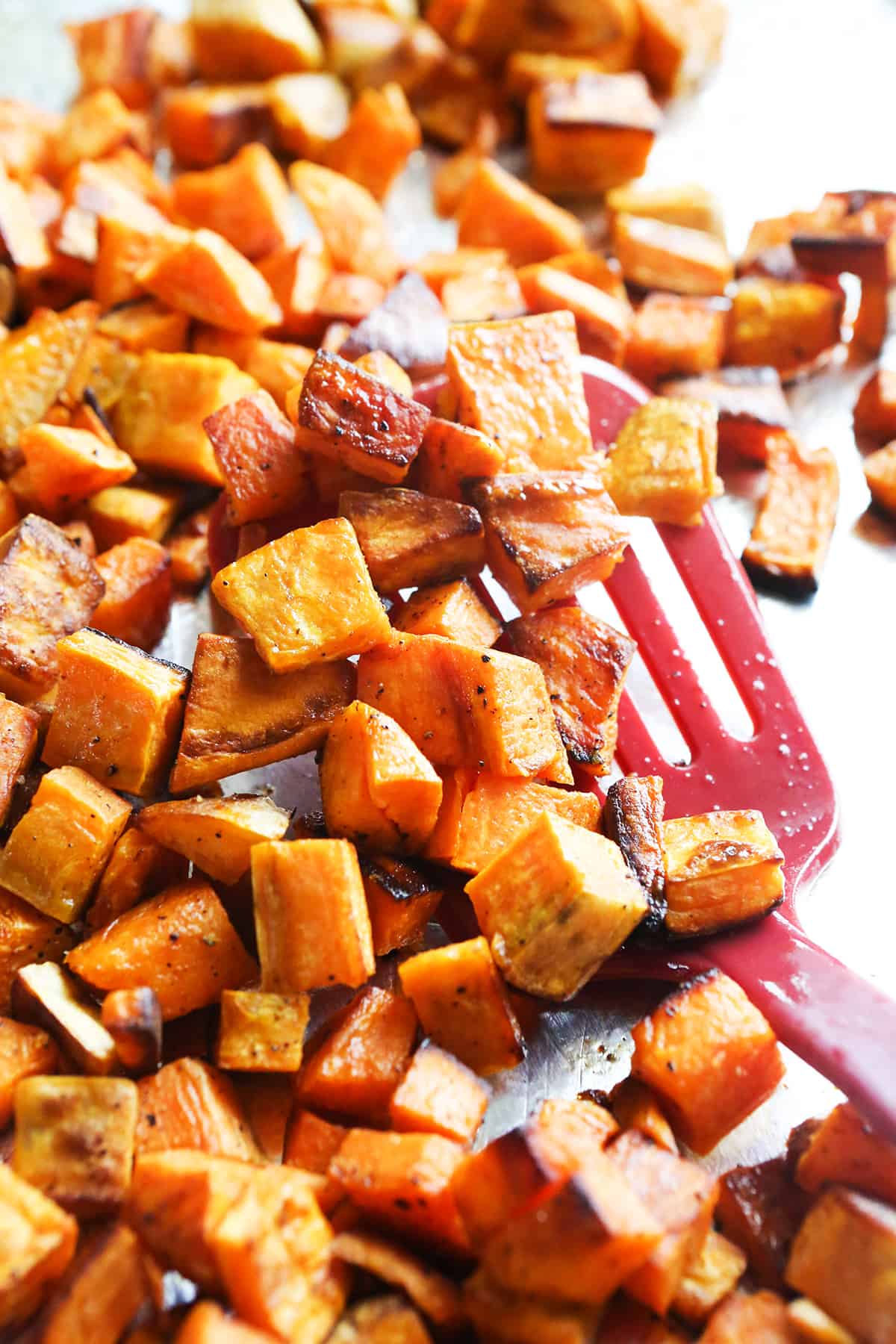 Roasted cubed sweet potatoes on a baking sheet with a spatula.