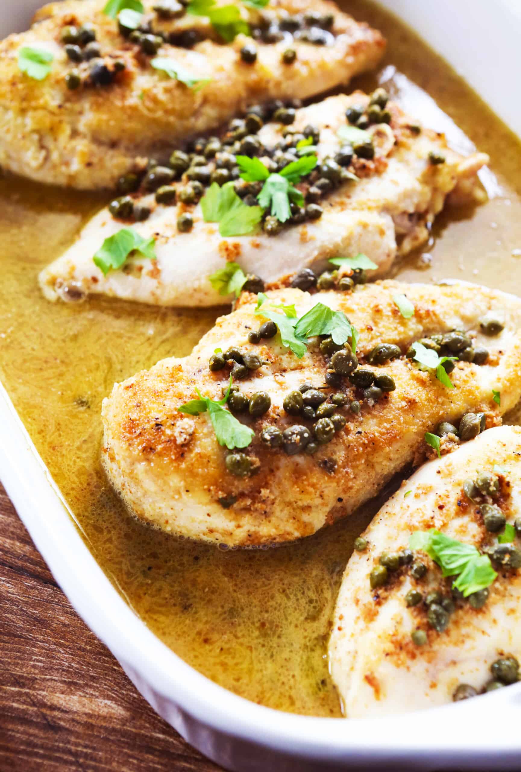 Baking dish with chicken piccata with lemon sauce and capers over the top. 