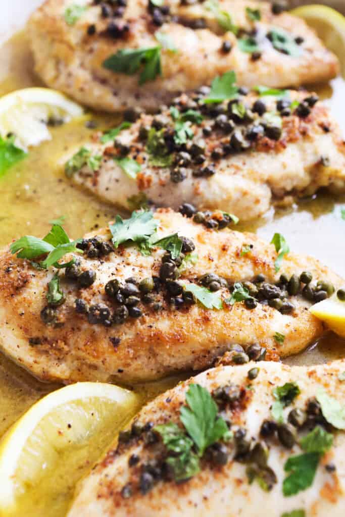 Lemon Chicken piccata sitting in a broth with capers on top and lemon slices as garnish. 