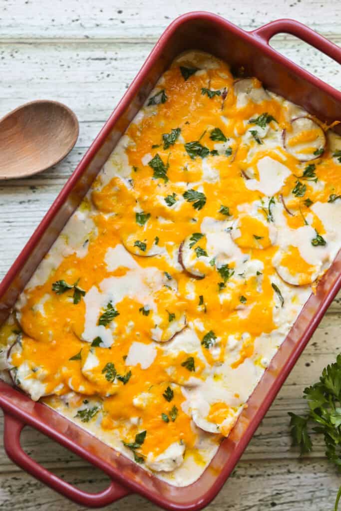 9x13 casserole pan filled with scalloped potatoes topped with melted cheese and garnished with parsley. 