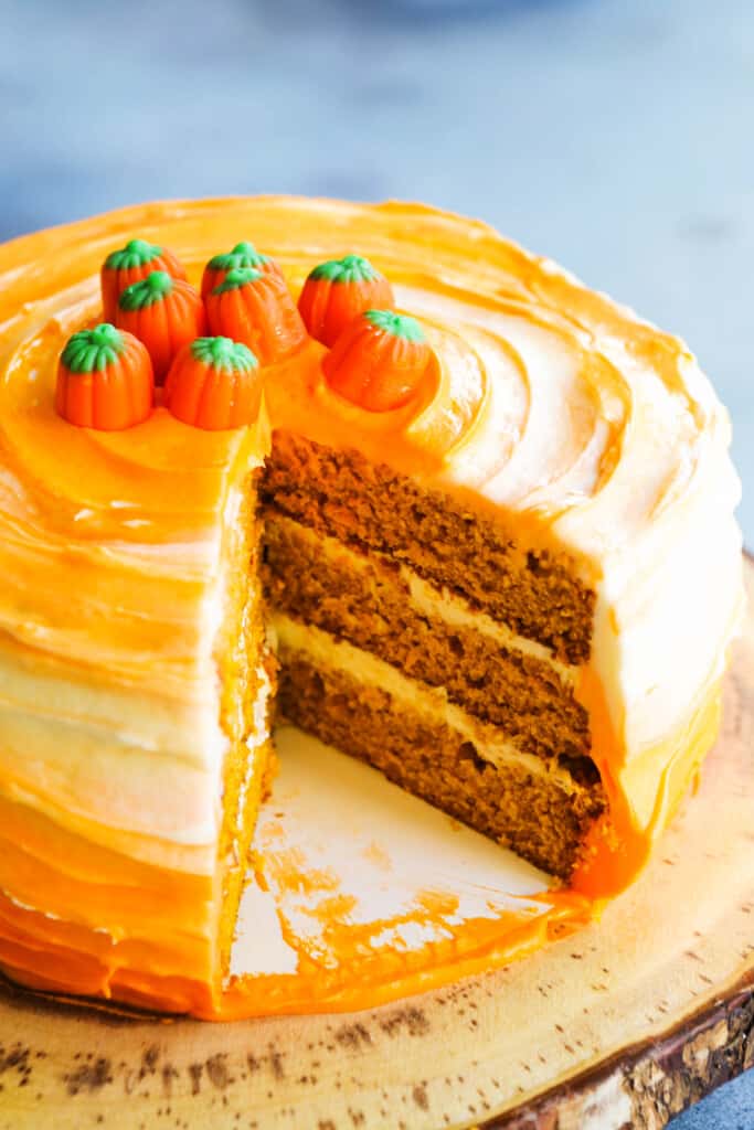 A pumpkin layer cake on a pedestal with a slice cut out showing the layers with frosting. 