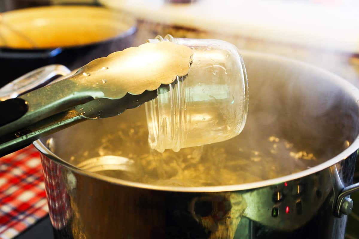 Tongs pulling a mason jar out of a pot of boiling water.