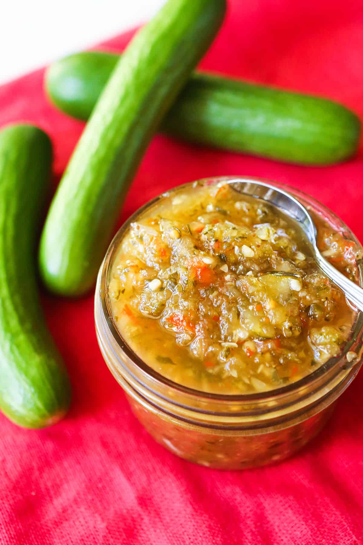Heaping jar of relish sitting next to cucumbers.