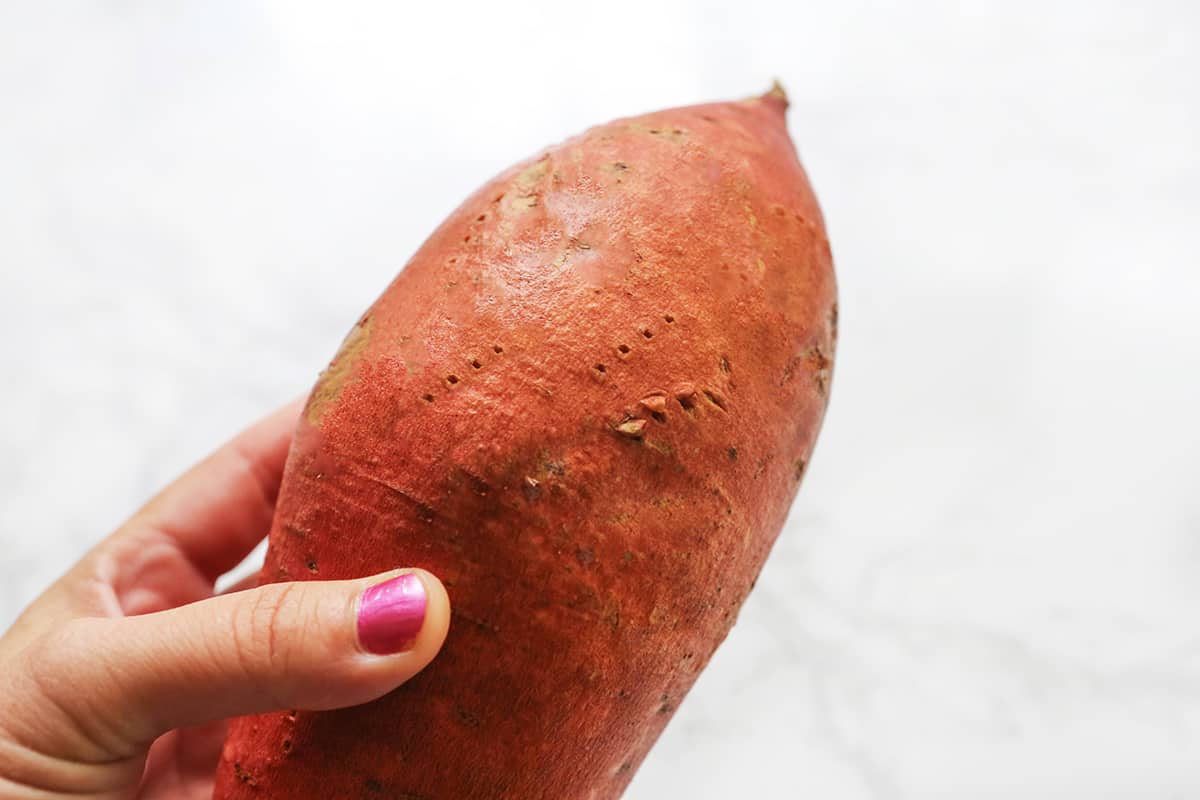 Hand holding a sweet potato with holed poked into the skin.