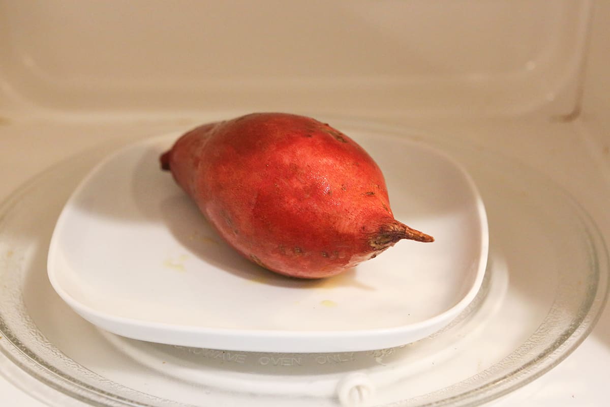Sweet potato sitting on a plate in a microwave.