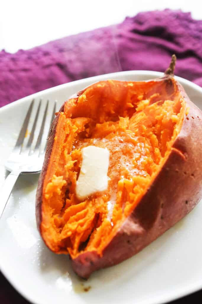 A sweet potato cut in half, mashed and a pat of butter melting on it. 
