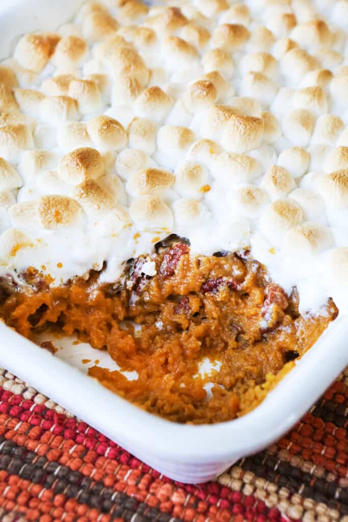 Sweet potato casserole topped with marshmallows and a scoop removed from the baking dish. 