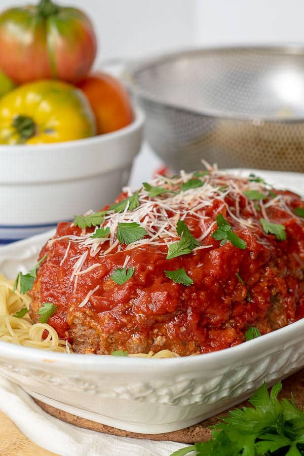White baking pan with Italian sauce on top of meatloaf sitting on a bed of pasta. 