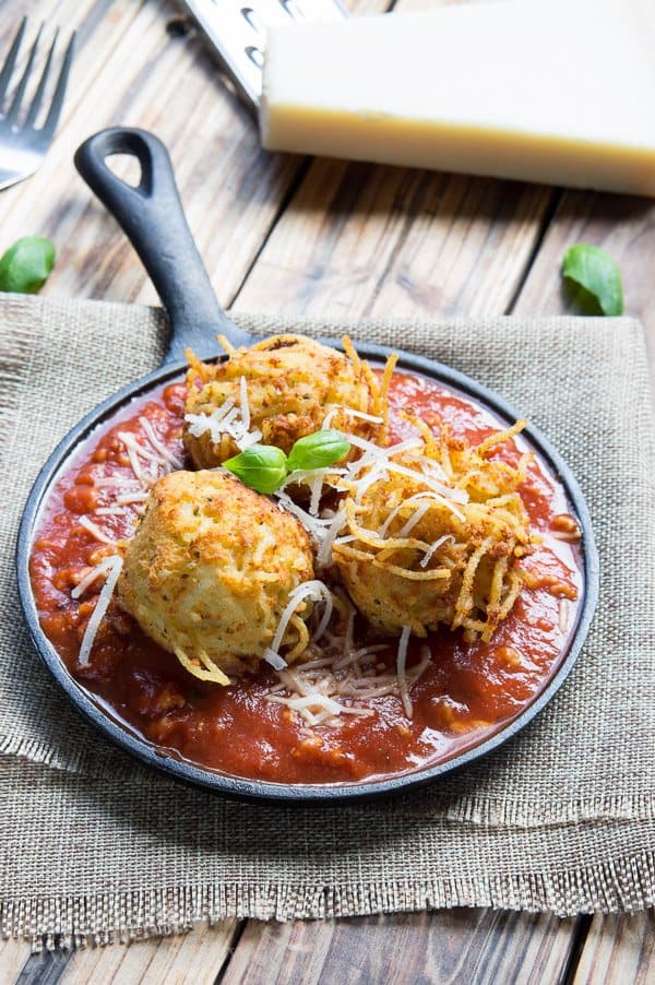 Two spaghetti balls sitting in a dish of spaghetti sauce. 