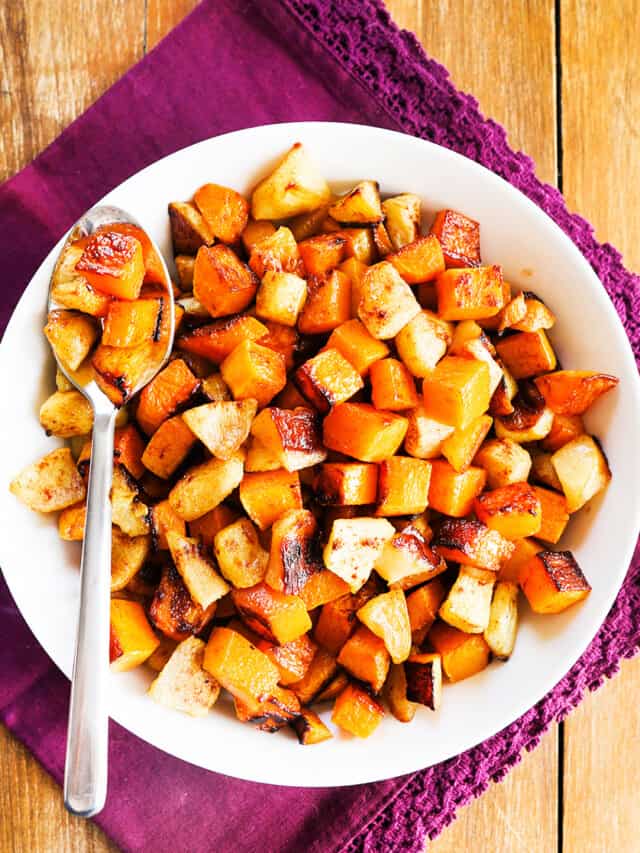 Serving bowl of butternut squash and apples with a spoon tucked in it. 