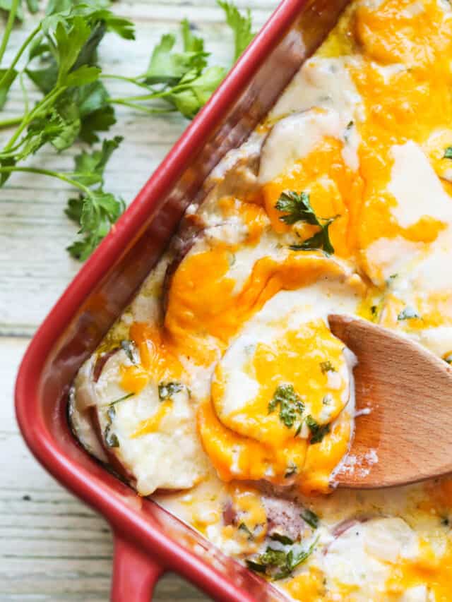 Wooden spoon sitting inside baking dish filled with scalloped potatoes.