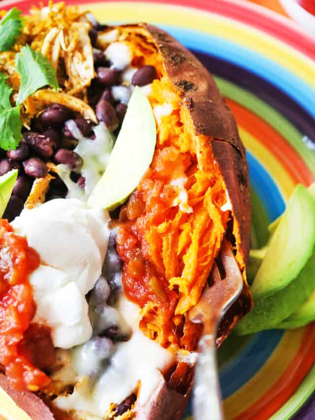 Stuffed Sweet Potatoes on a plate topped with sour cream, salsa, black beans and cilantro. 