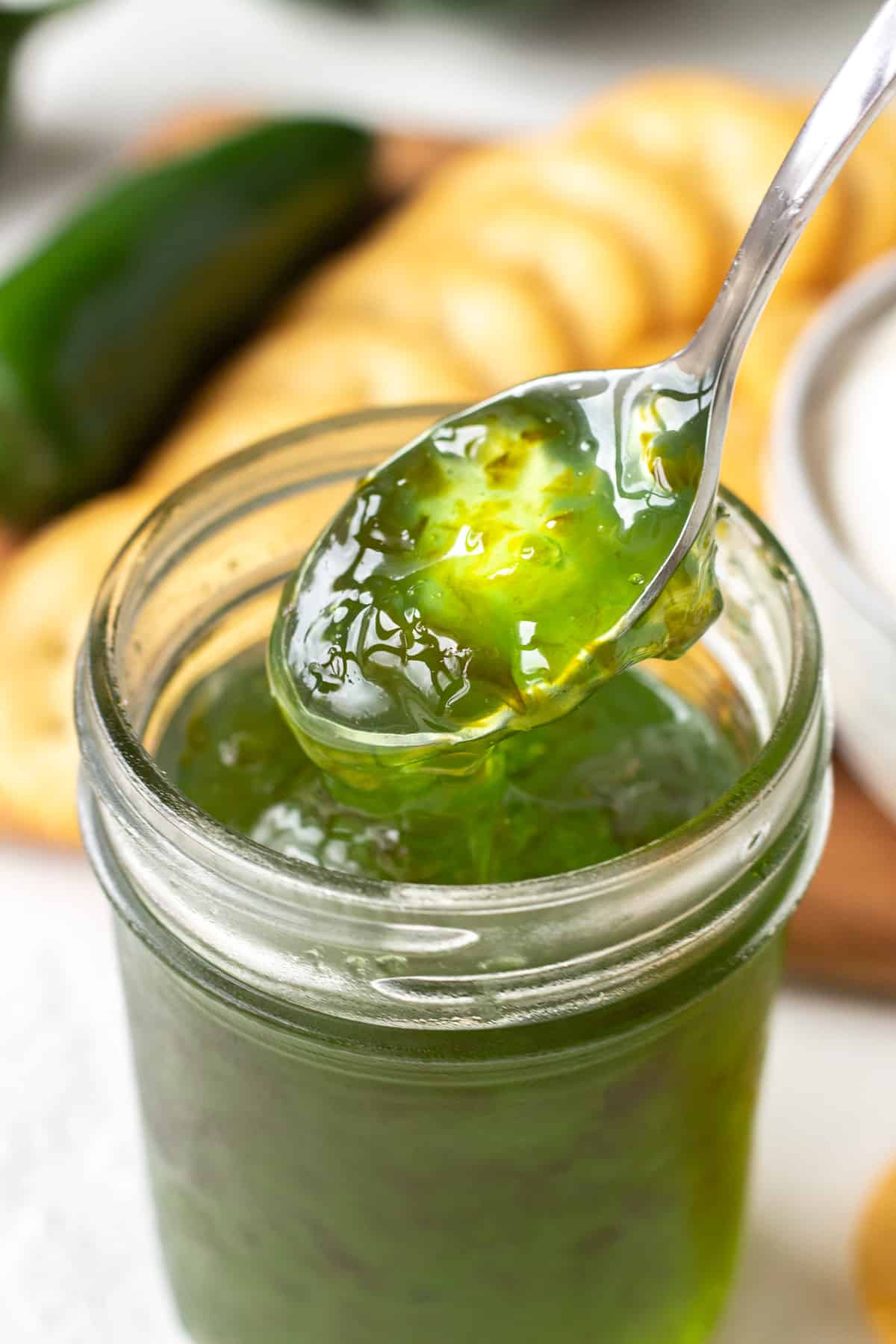 Spoon lifting green pepper jelly out of a mason jar surrounded by Ritz crackers.