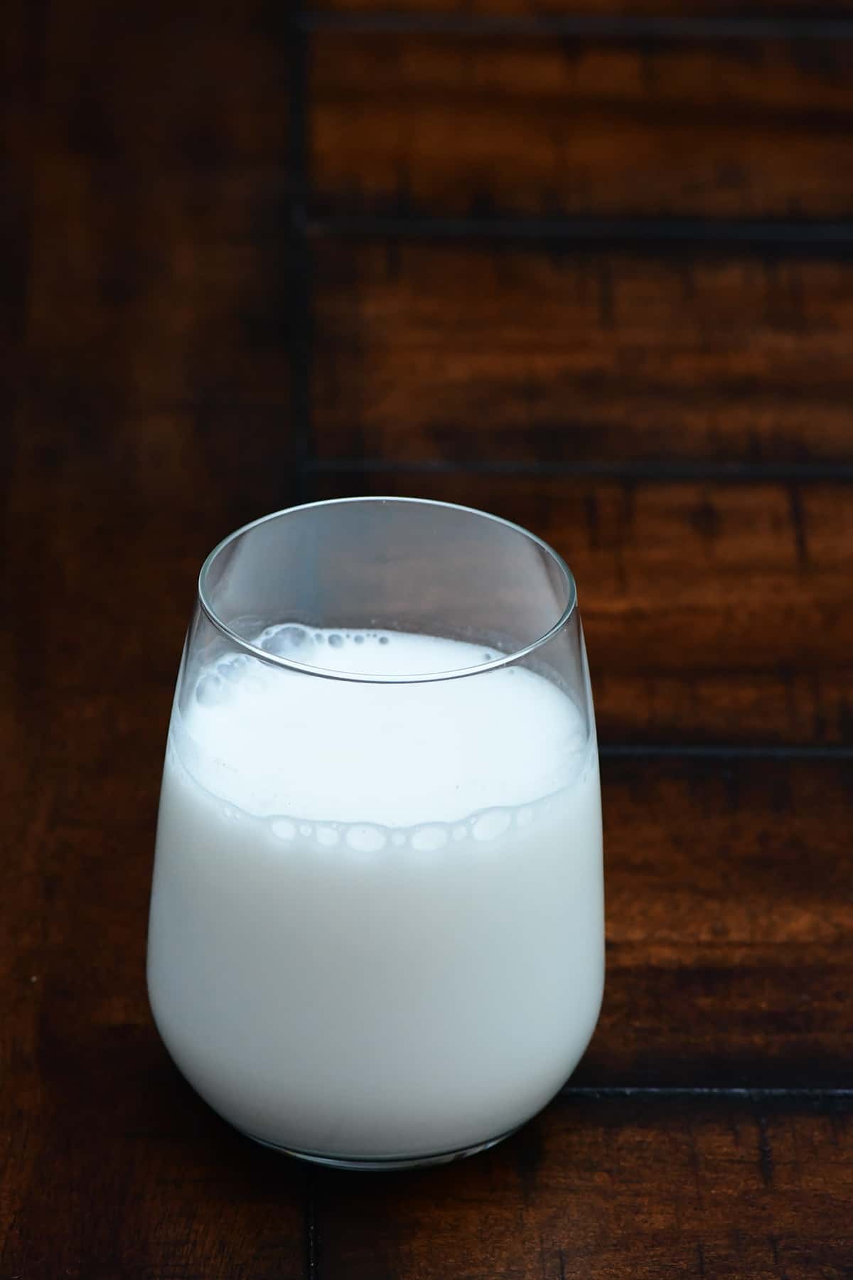 Glass of milk sitting on a dark wood table.