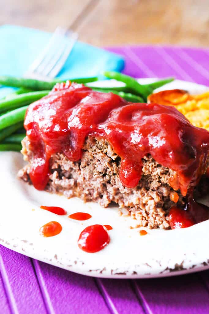 A plate with fresh green beans and a slice of meatloaf with red sauce drizzled over the top. 