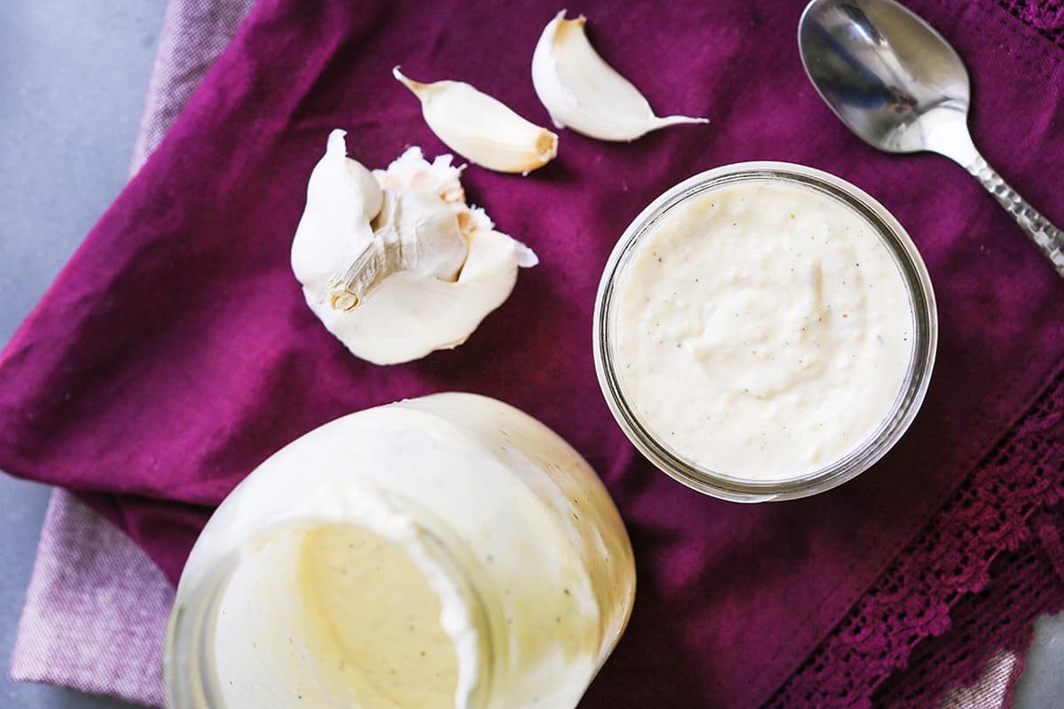 Looking down into a jar of alfredo sauce, next to garlic and a spoon.