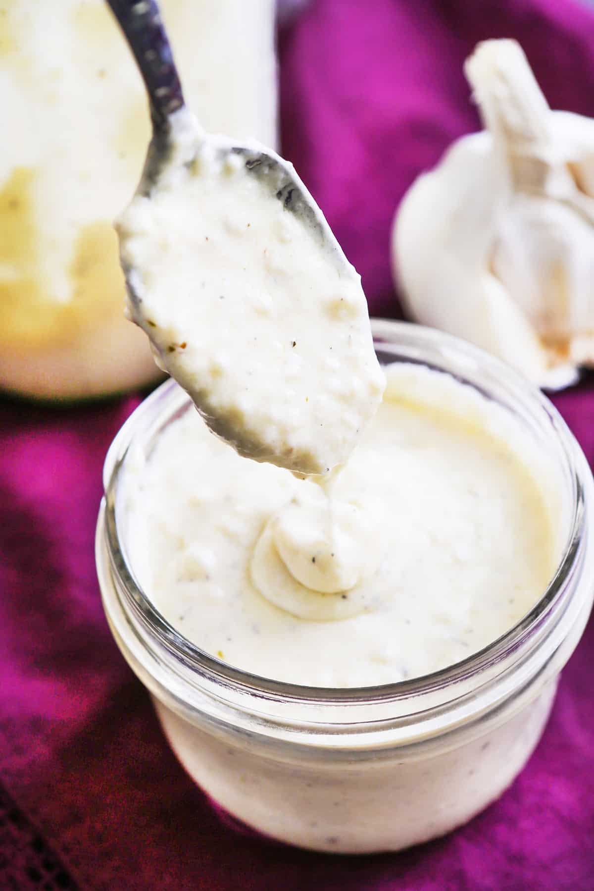 Spoon being held over a mason jar full of Alfredo sauce.