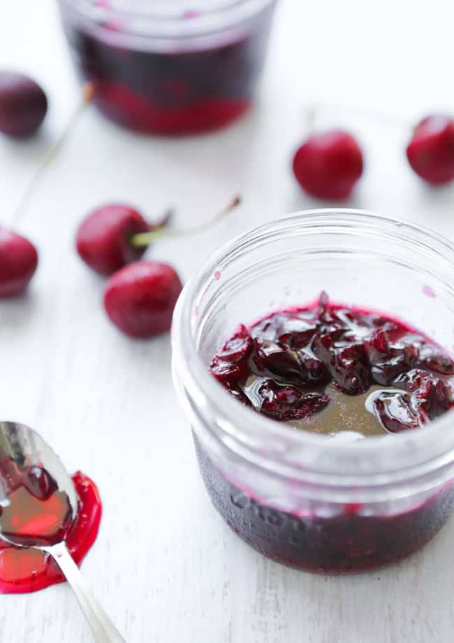 Cherry jam in a small mason jar surrounded by fresh cherries.