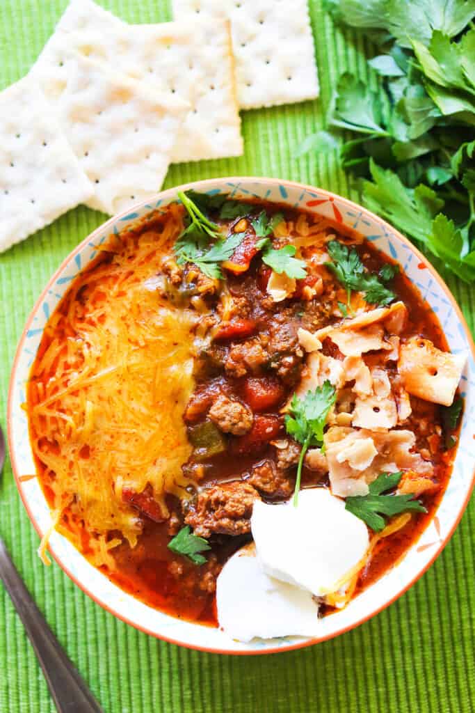 Bowl of chili with all the toppings and sitting next to saltine crackers.