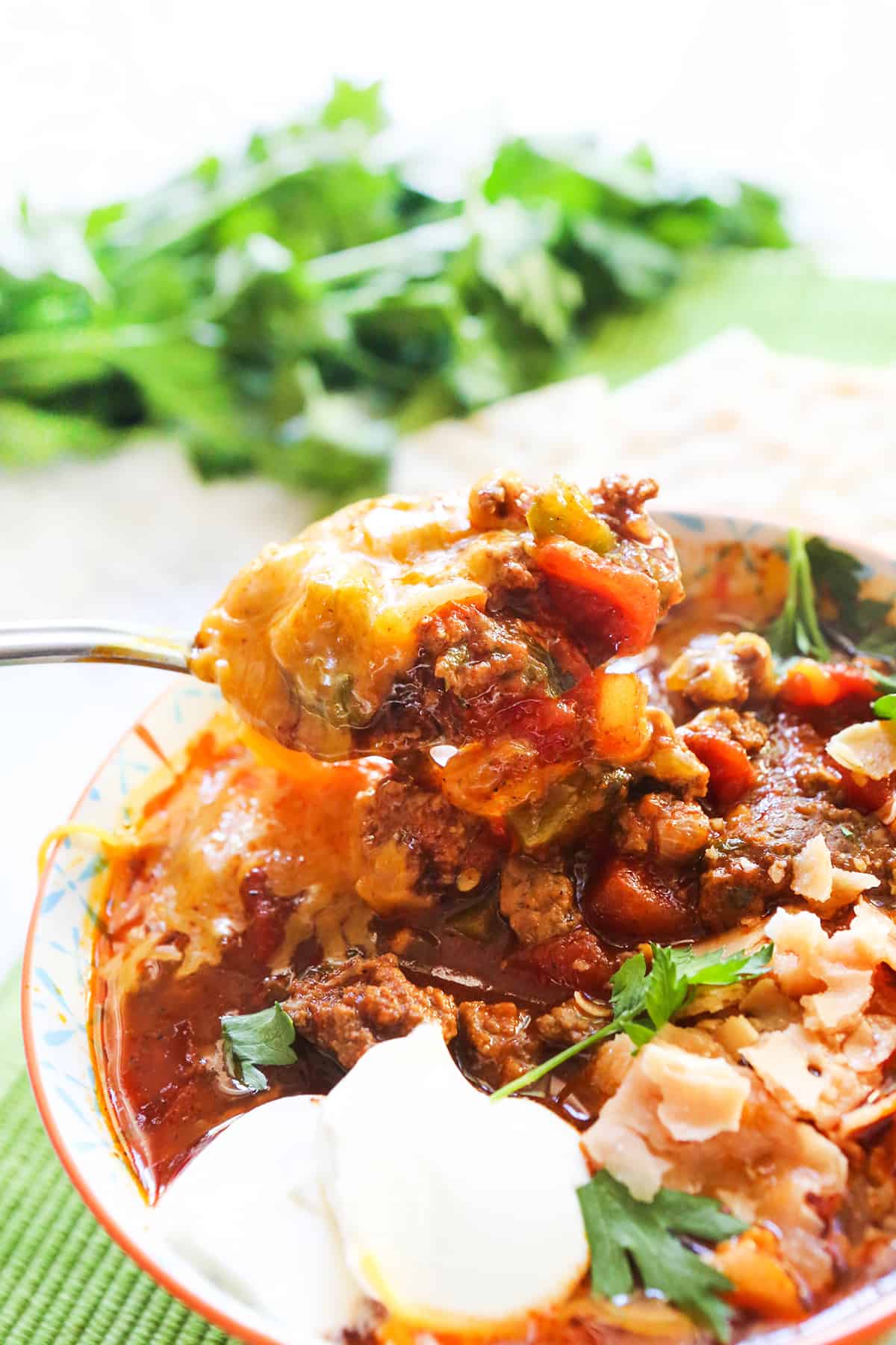 Spoon pulling a meaty, cheesy bite of chili without beans out of a bowl.