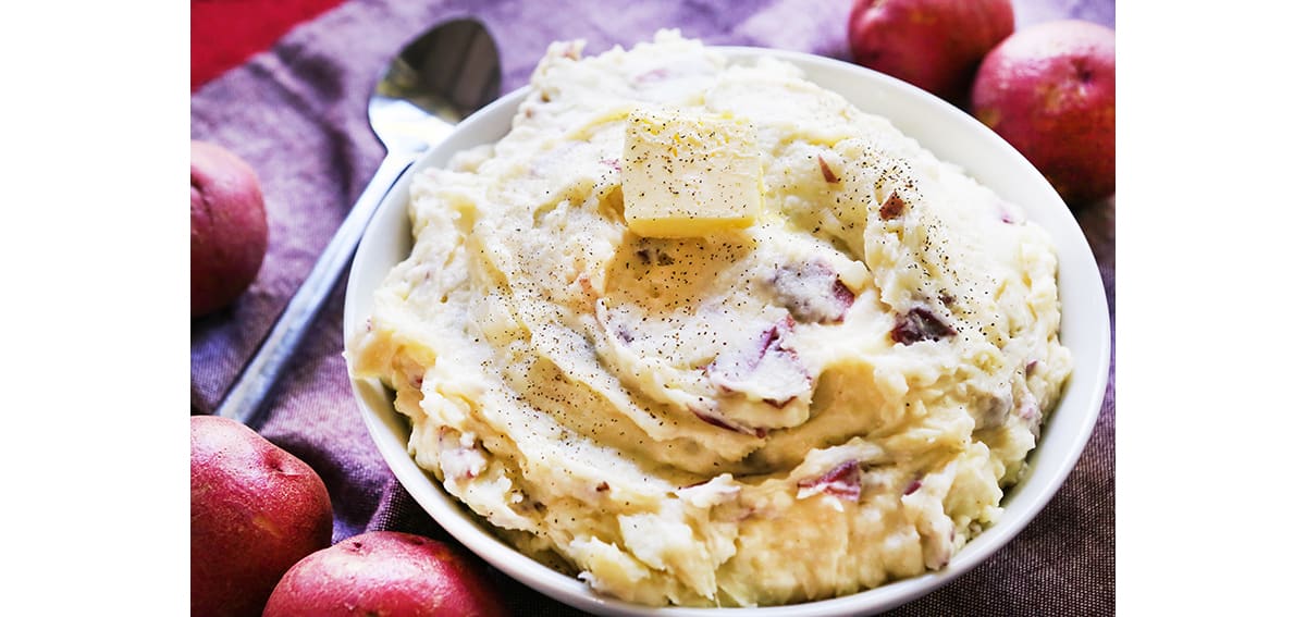 Serving bowl filled with mashed potatoes and a pat of butter on top.